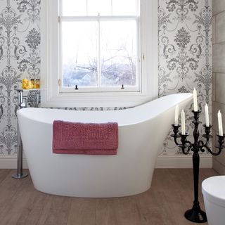 bathroom with white designed wall bathtub with towel white window and candle stand