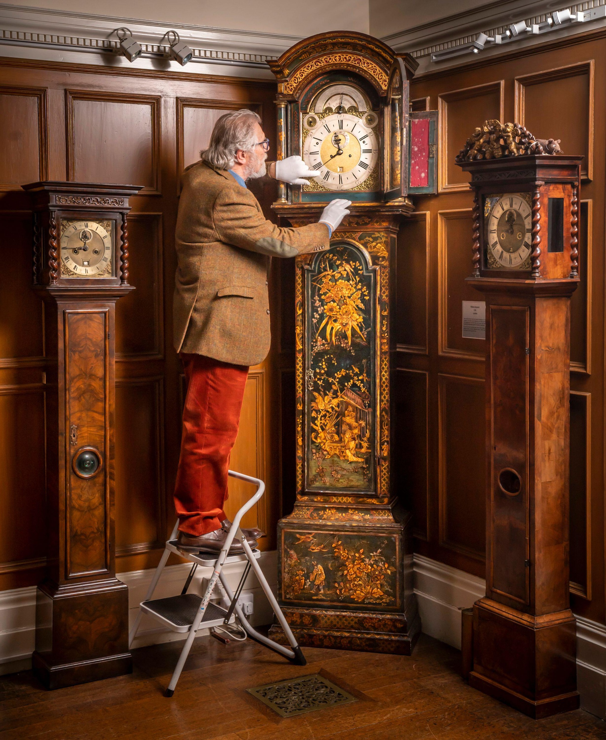 A man sets a large grandfather clock in a room full of other grandfather clocks