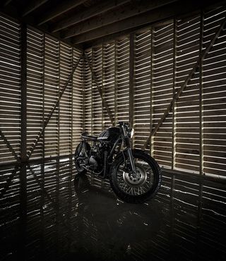Interior view of the wooden garage at Float House. There is a black motorcycle sitting on the dark coloured flooring