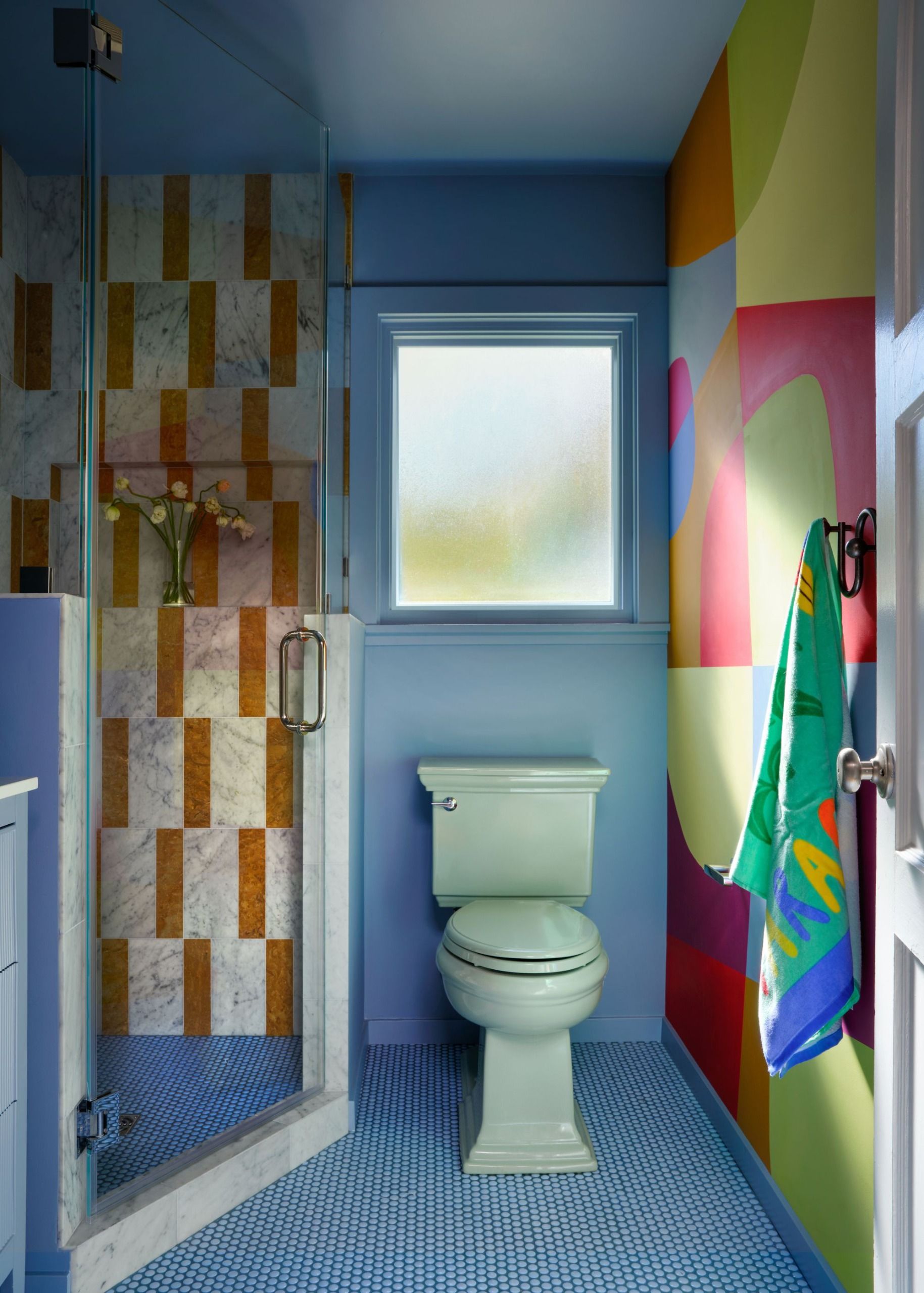 A bathroom with blue walls, blue floor tiles, and a multicolored mural 