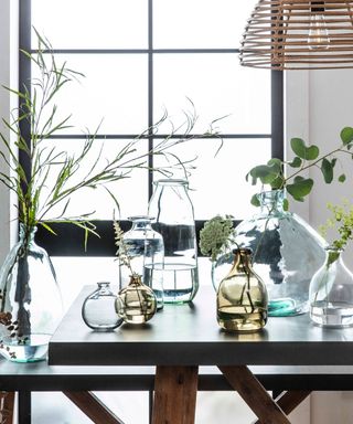 clear glass bottle vases sat on a wooden dining table with a window beyond