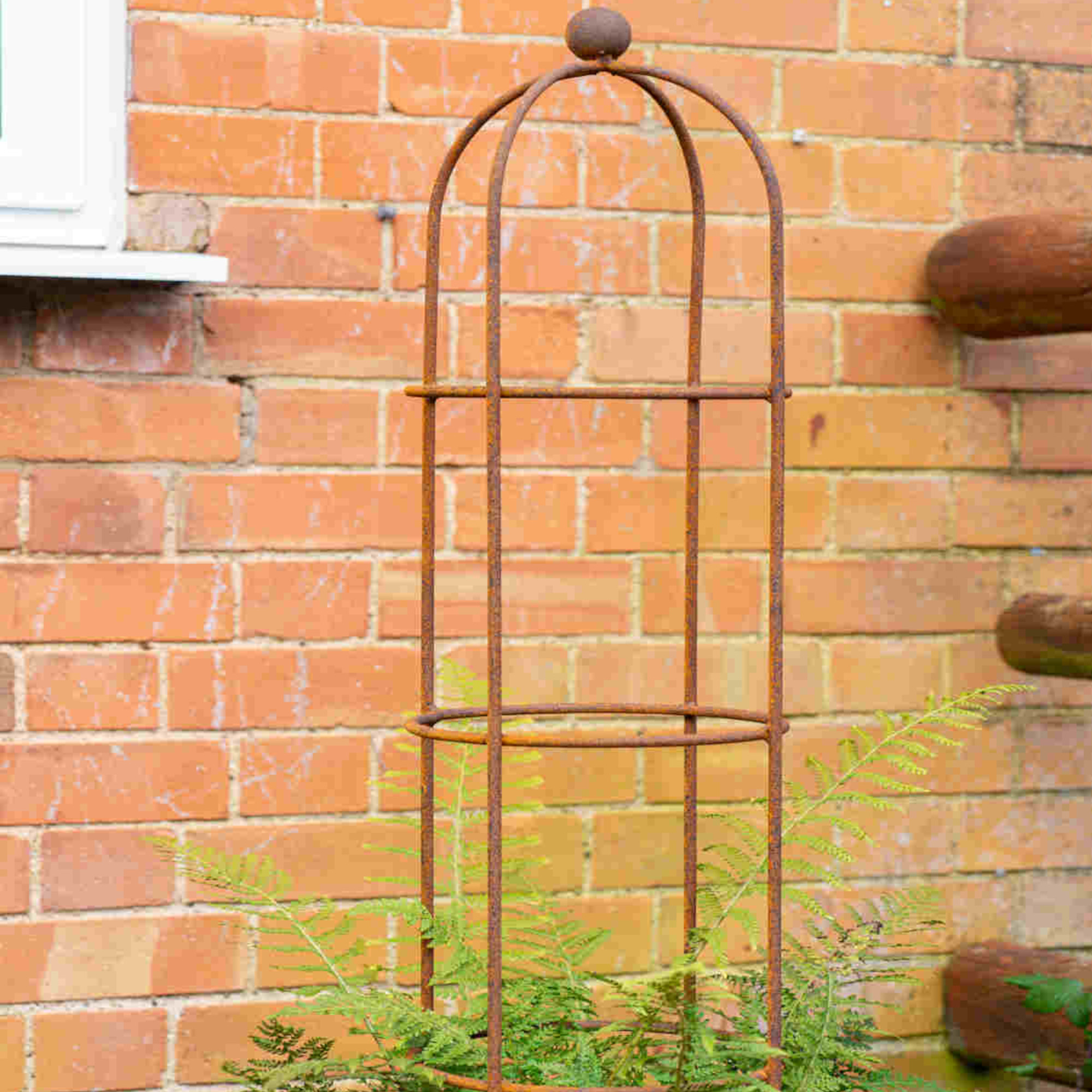 Hayloft round obelisk supporting a fern near a brick wall in a garden