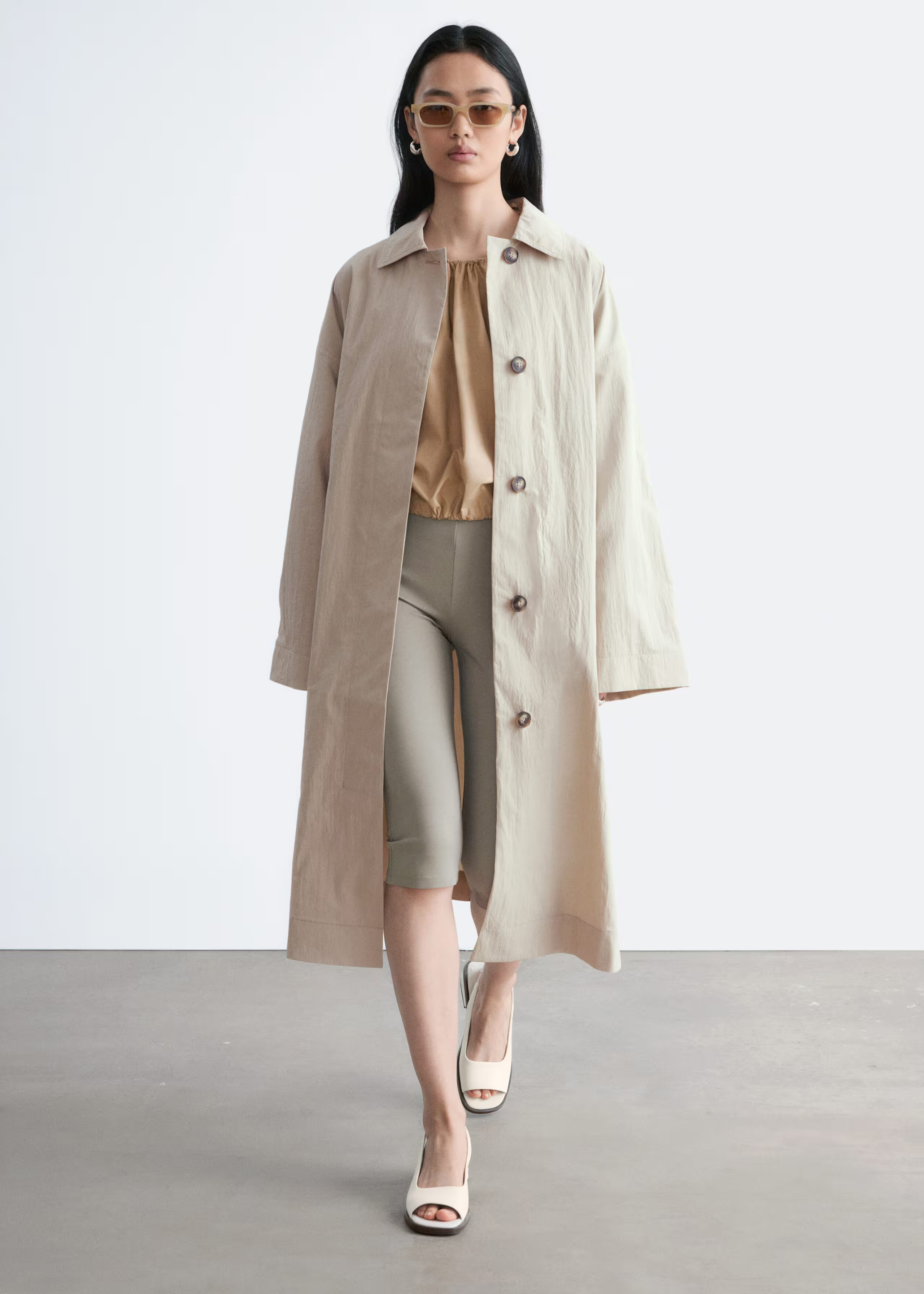 An image of a model wearing a beige trench coat and khaki capris
