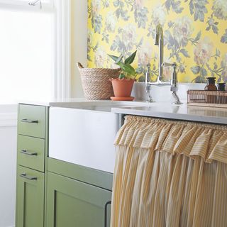 kitchen sink area with green kitchen cabinets, orange cafe curtains, a white sink and a plant next to the sink