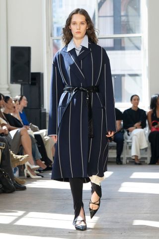 model wears black leggings with a blue button-down blouse and striped trench coat in Proenza Schouler spring 2025