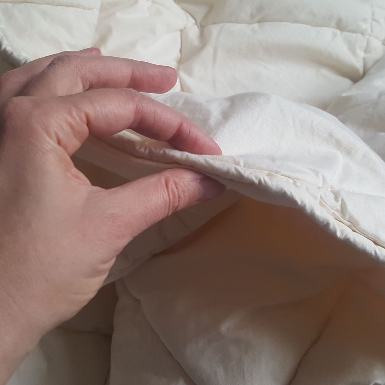 The woolroom mattress protector held between a person's thumb and forefinger