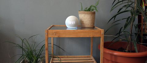 Amazon Echo Dot with Clock (2020) pictured on a wooden table next to a plant.