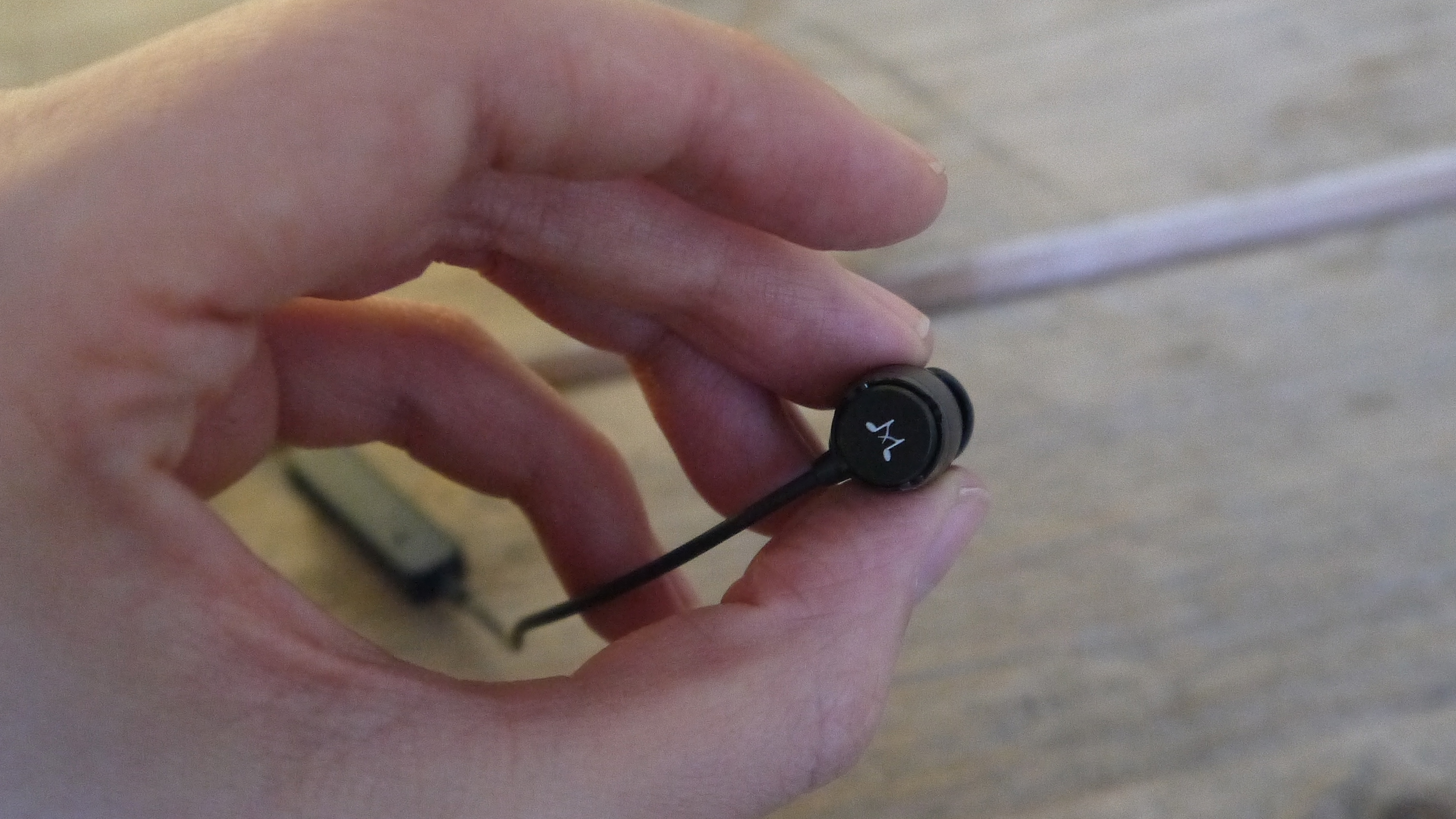 En person som håller i ena hörluren på ett svart par SoundMAGIC E11BT