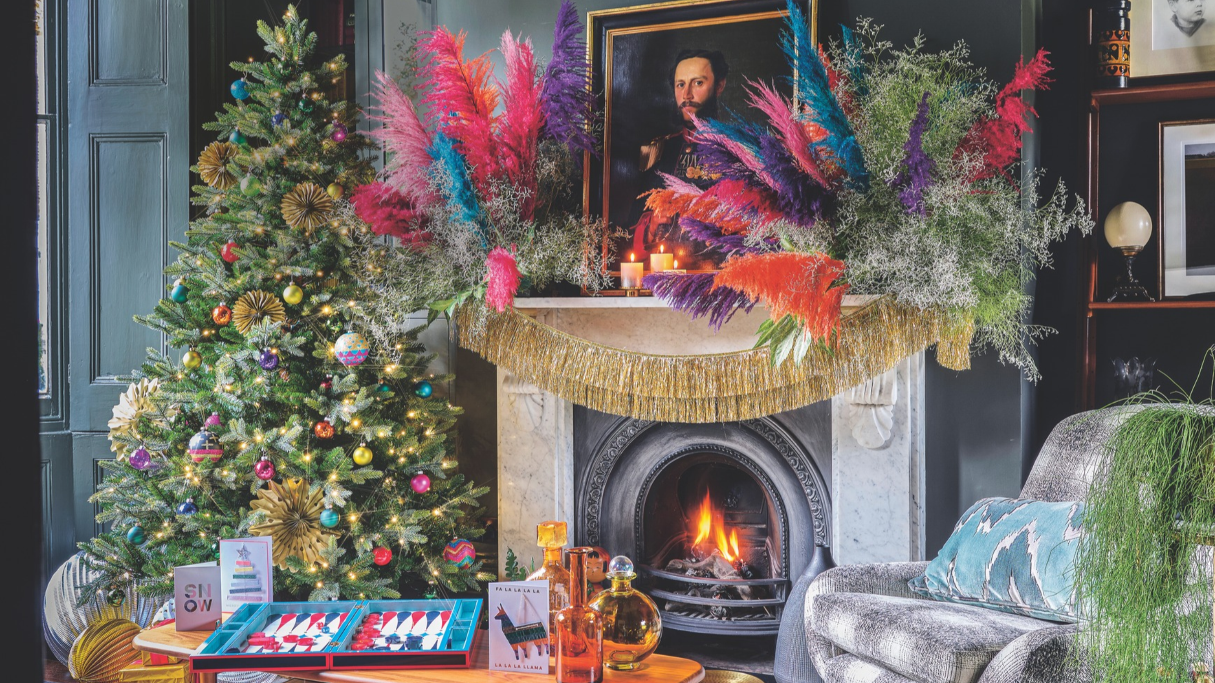 Living room with decorated Christmas tree beside decorated lit fireplace and mantelpiece with coloured grass decoration.