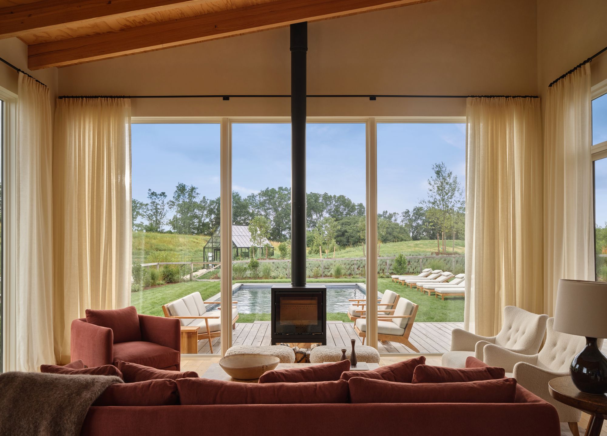 living room with burnt orange furniture, a tall wooden ceiling, and a wood burning fireplace looking out to a large backyard with a pool