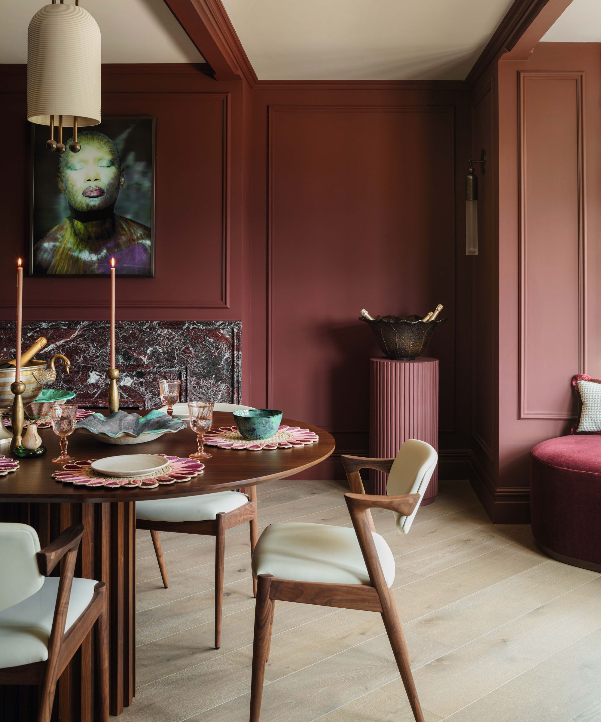 a dark moody red dining room with a rosso red marble fireplace and dark wood round table and chairs