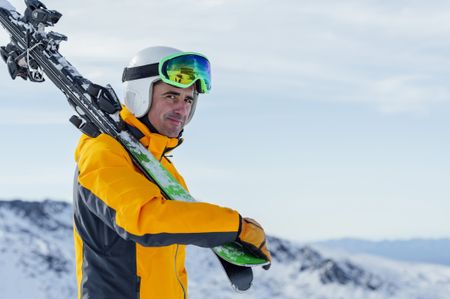 A smiling man in his 40s or 50s is carrying his skis and looking at the camera