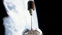 a barrel-shaped satellite is seen departing the payload bay of a space shuttle in Earth orbit