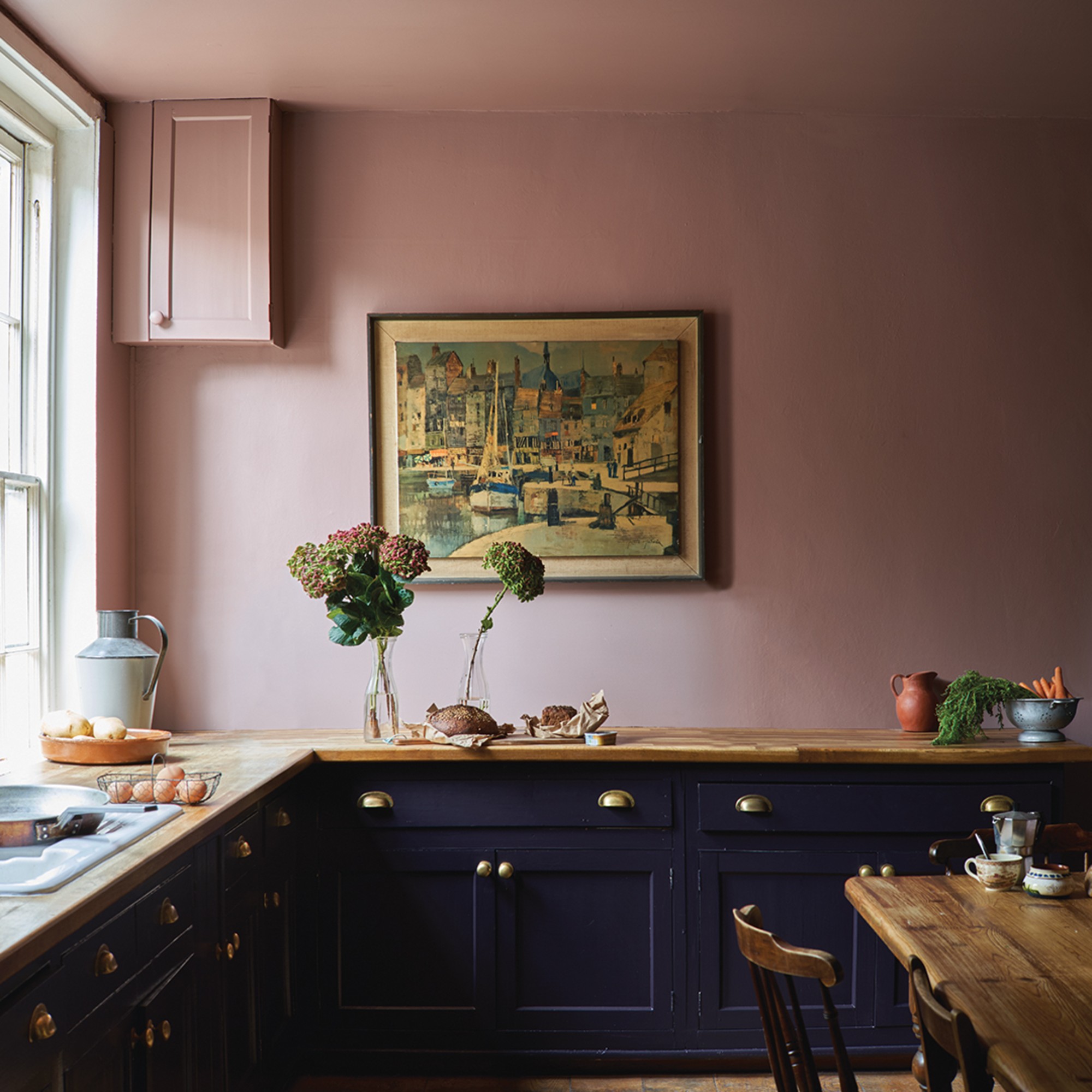 A kitchen with black cabinets and pink walls painted in Farrow &amp; Ball&#039;s Sulking Room Pink