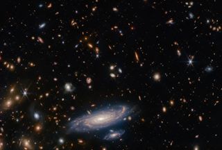 A bright spiral galaxy appears on a background of thousands of other distant galaxies