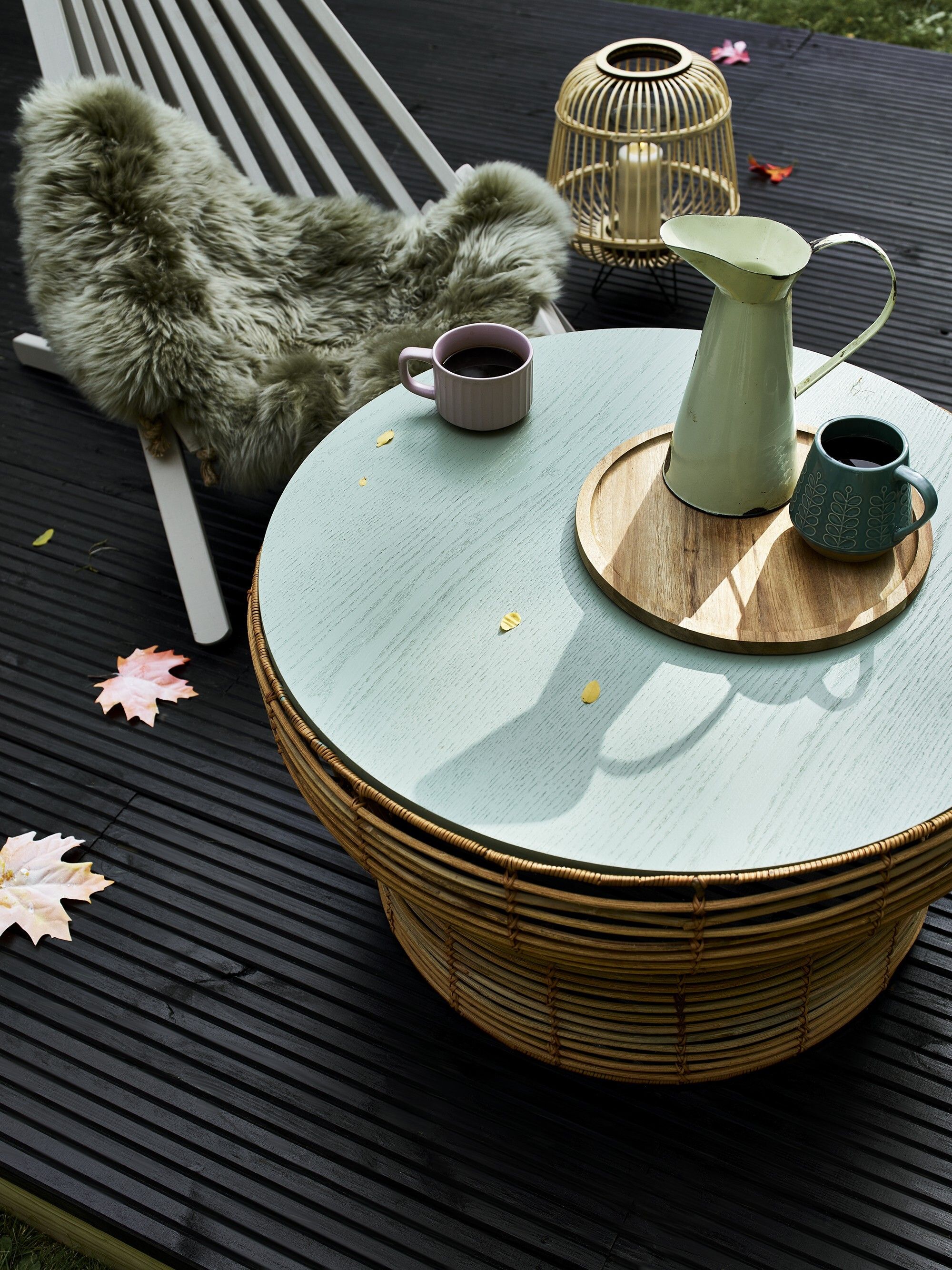 Image of a wicker coffee table with the top painted in a light teal on a black deck