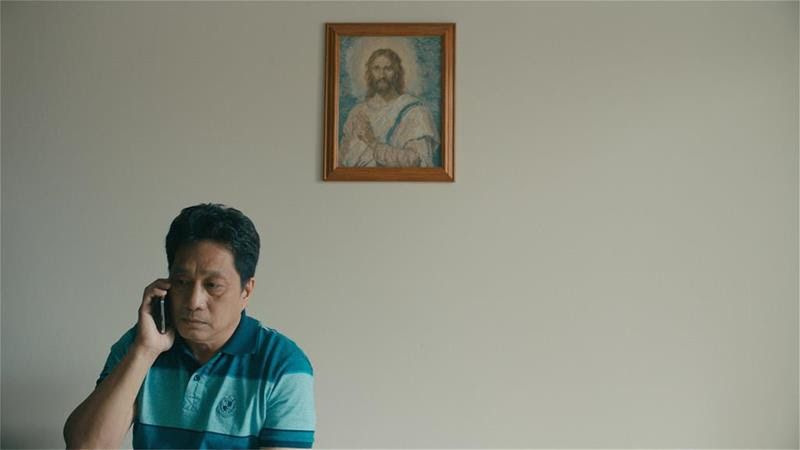 Joshua (Rogelio Balgatas) on the phone, under a painting of Jesus