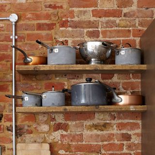 Pots and pans stored on shelves against exposed brick wall