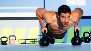 Man performing a push-up with two kettlebells during outdoor workout