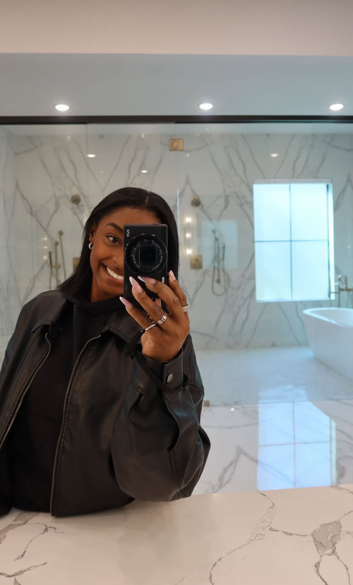 a black woman taking a bathroom mirror selfie with a digital camera
