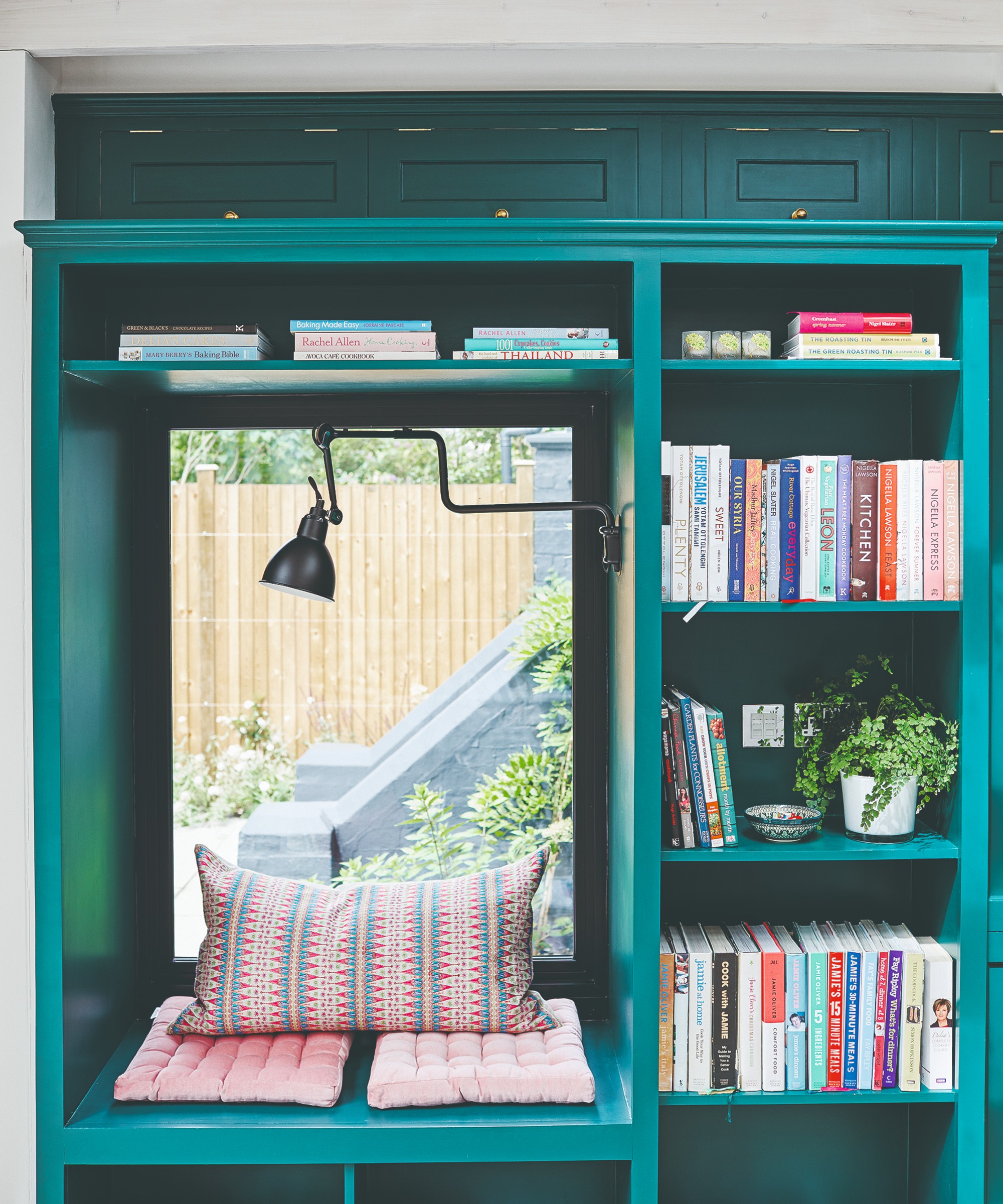 A teal-painted window seat with a built-in bookcase