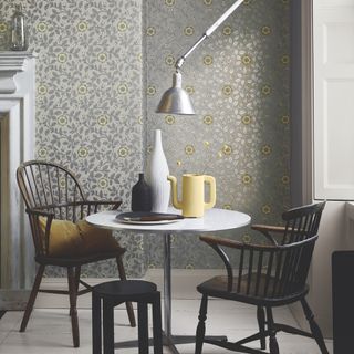 small dining room space with metallic grey and yellow wallpaper, Windsor chairs with small white table, vases, wall mounted lamp, fire place