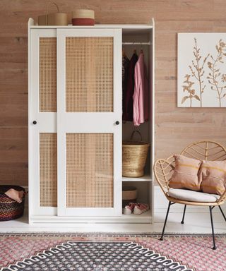 A white and cane closet with leaf-shaped rattan chair, wood-effect wallpaper, and white canvas wall art with biophilic detail