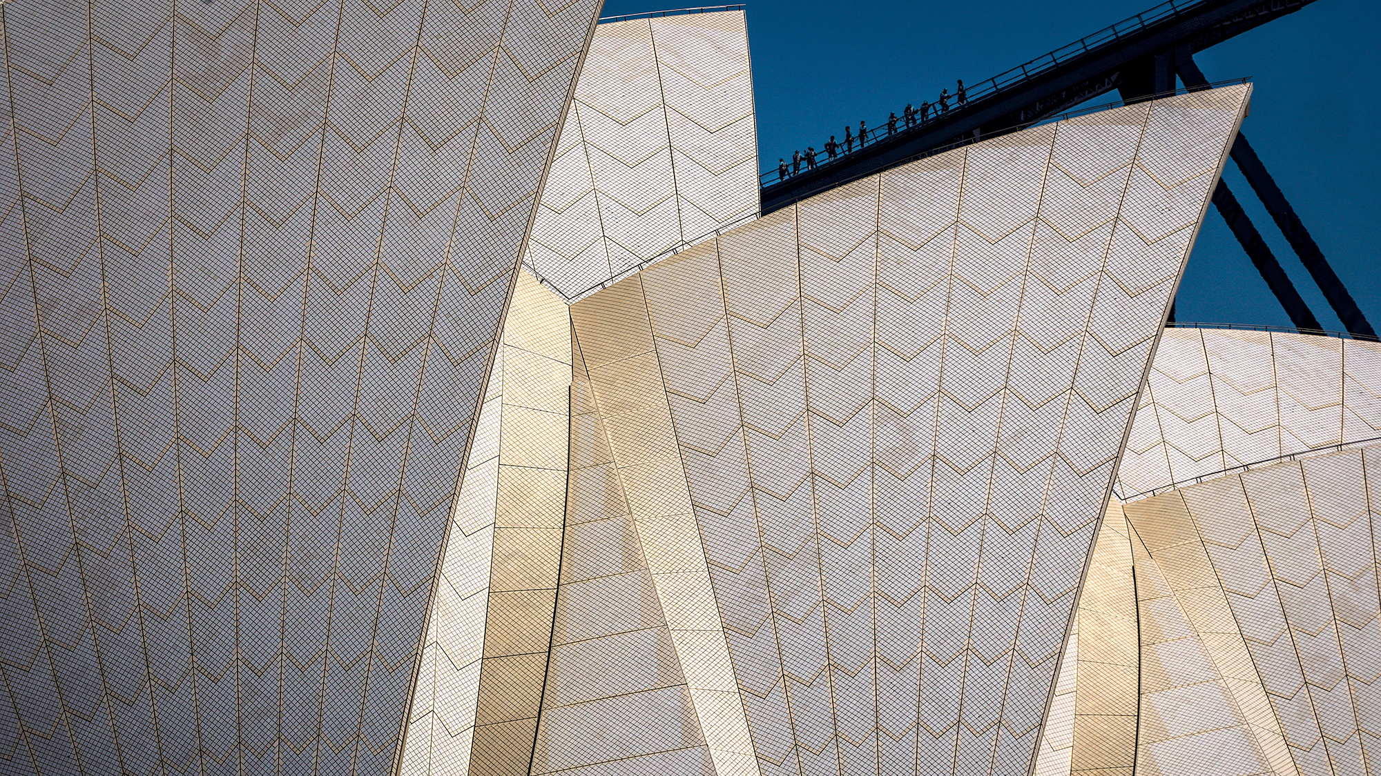The sails of Sydney Opera House frame a group of tourists ascending Harbour Bridge in Sydney, Australia