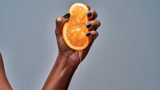 woman squeezing orange on grey background