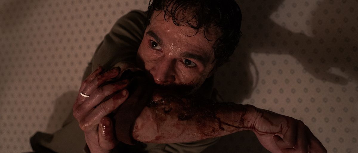 Christopher Abbott as Blake chewing on his injured arm in Wolf Man