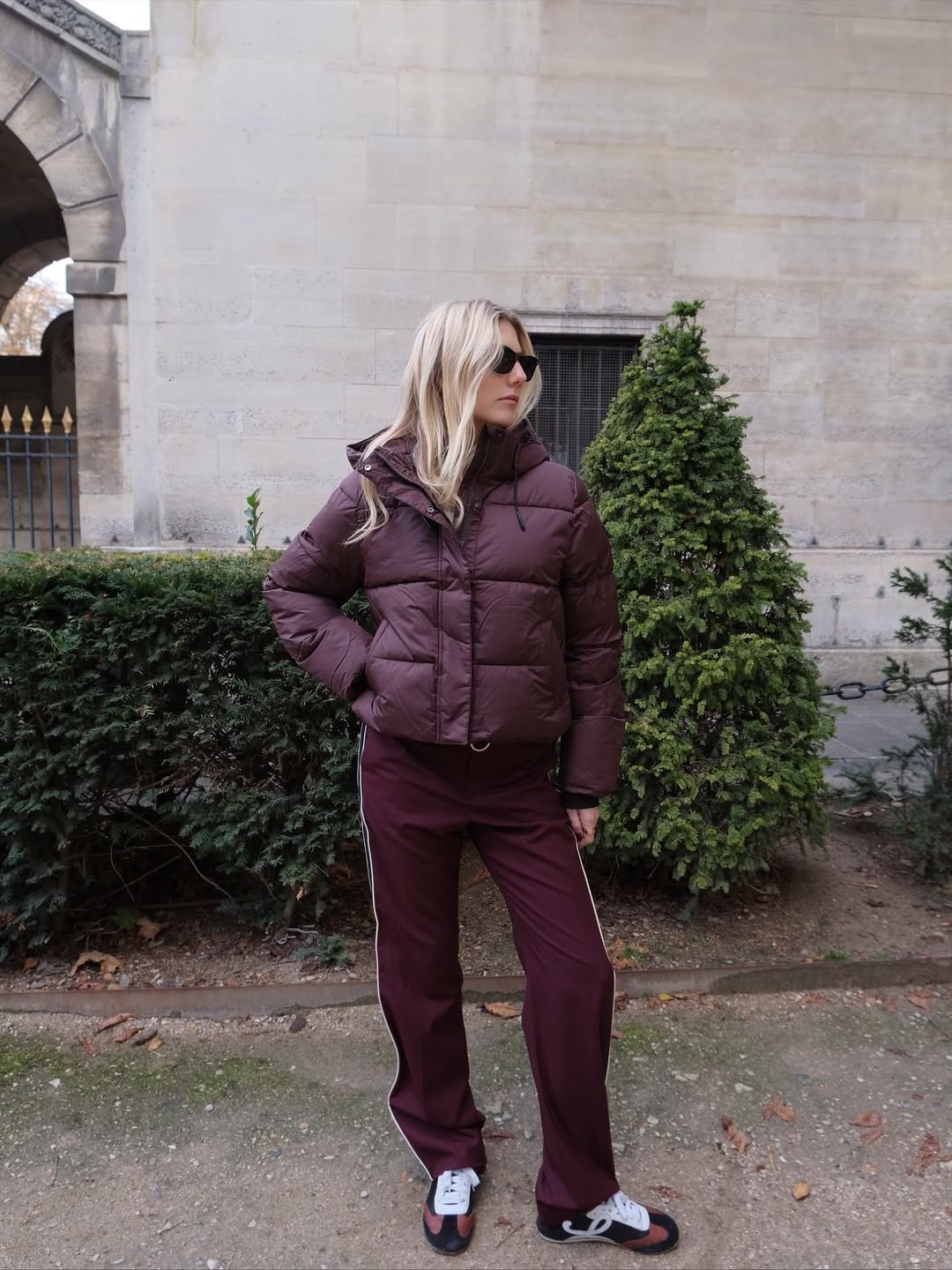 Lilly Sisto wears a puffer jacket, track pants and trainers that are all burgundy.
