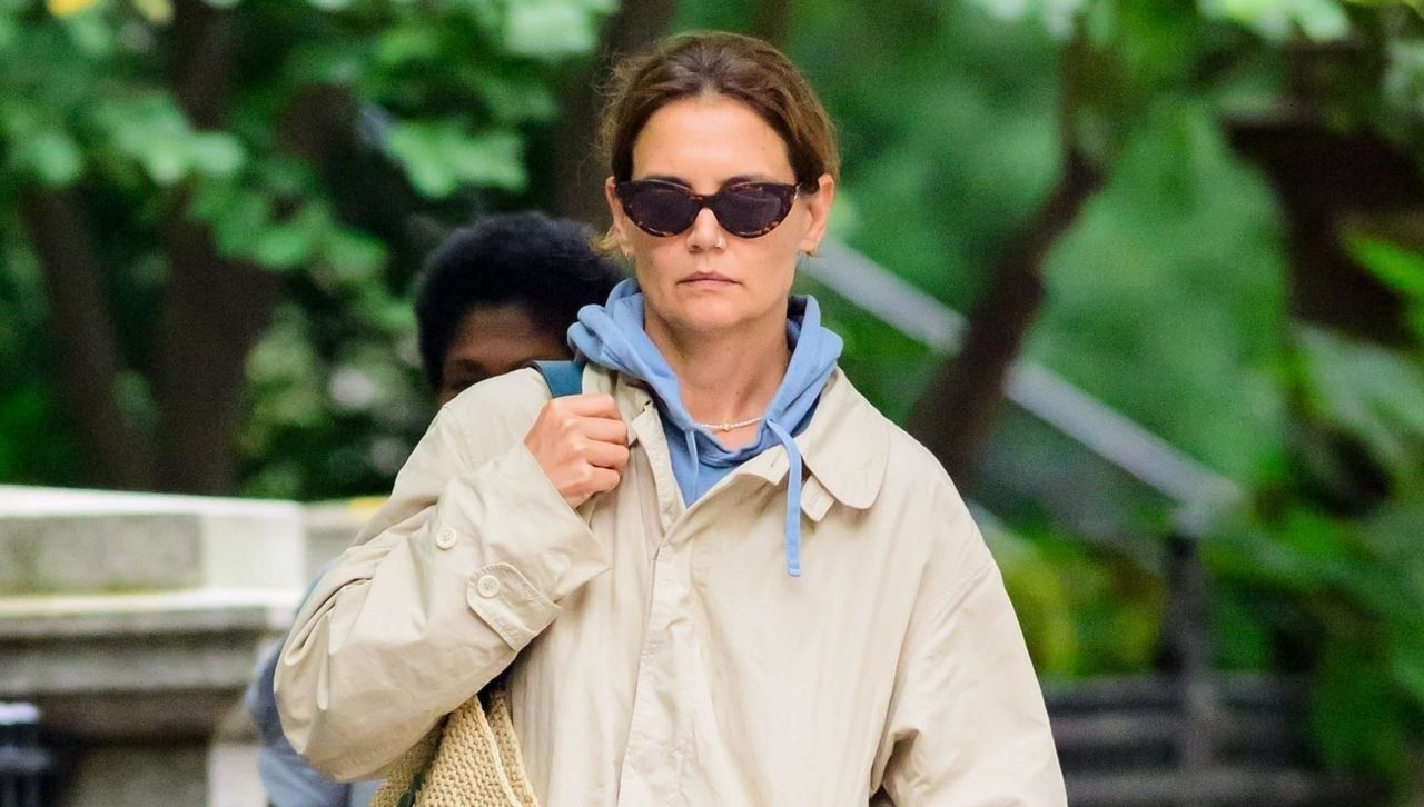 Katie Holmes walks in the New York City rain wearing a trench coat and a blue hoodie