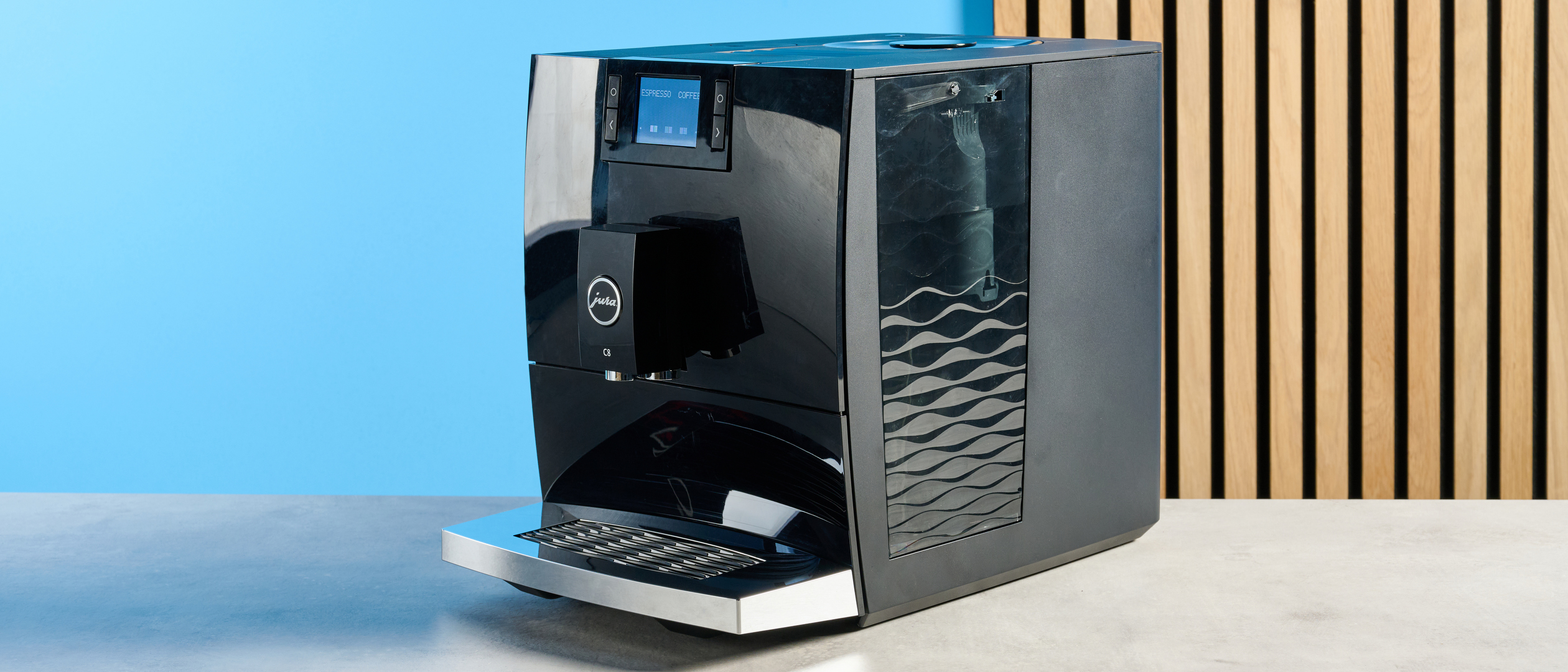 the jura c8 automatic coffee machine in piano black photographed with a blue and wood background