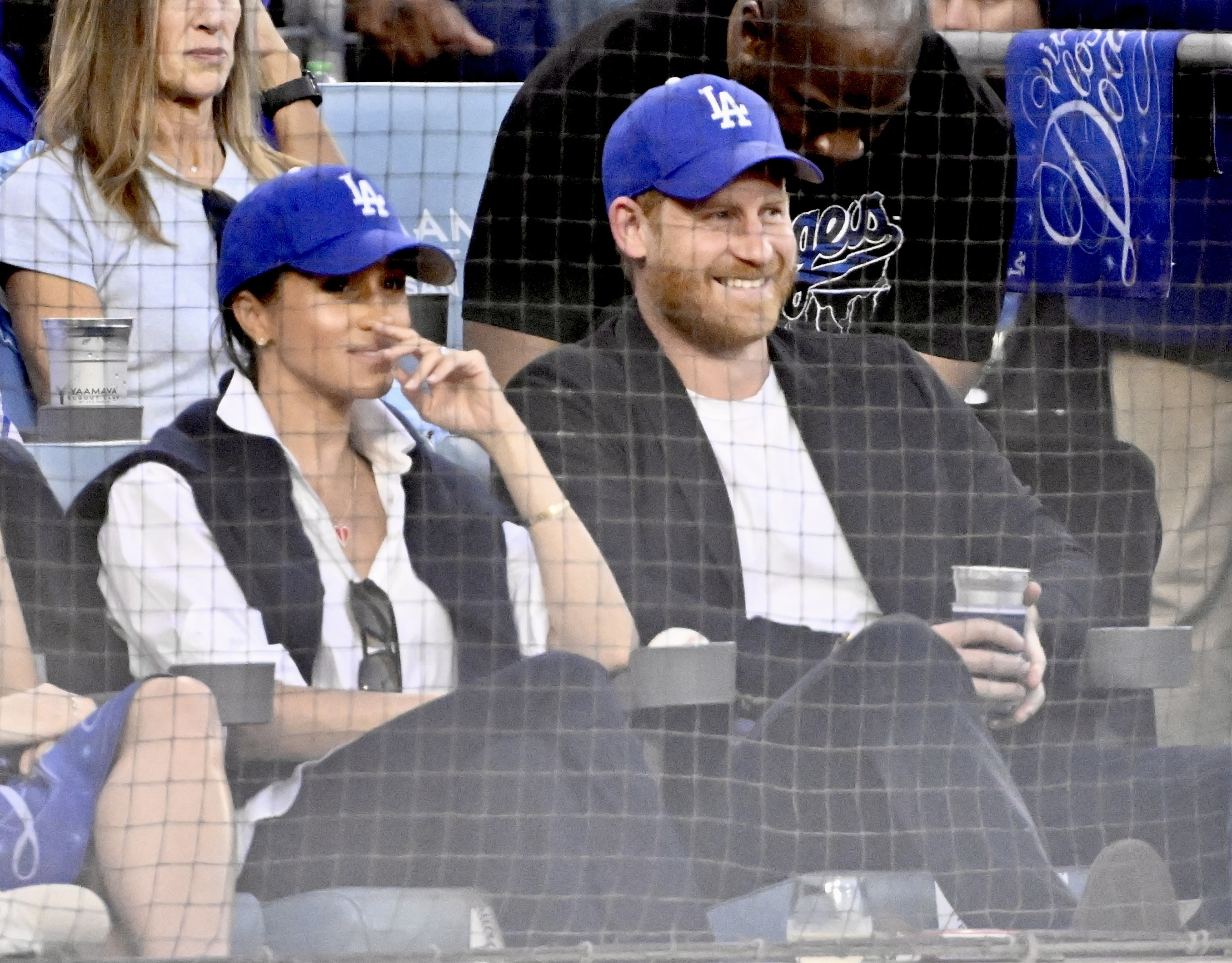 Meghan Markle and Prince Harry sitting in seats wearing Dodgers hats at the World series
