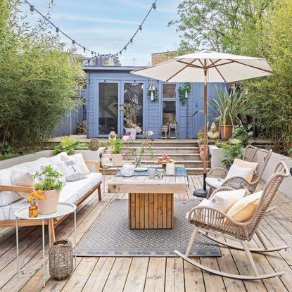 Decked garden with steps leading to a blue painted summerhouse and outdoor seating