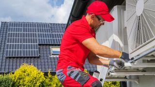 heat pump installer on ladder working on heat pump