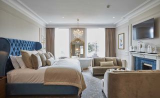 Fawn-coloured bedroom with blue headboard and fire surround and a chandelier