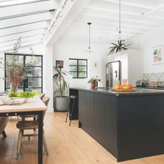 Side return kitchen extension with white walls, wood flooring, black kitchen island and fixed rooflights overhead