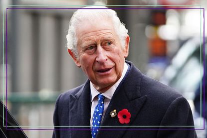 a close up of King Charles III wearing a black coat with a poppy