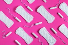 A bright pink background displays an arrangement of white tampons and sanitary towels.