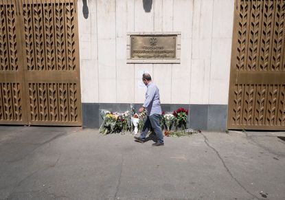 A man walks past flowers placed outside the Russian embassy in Tehran, Iran, to honor the victims of a shooting at the Crocus City Hall concert venue near Moscow, Russia