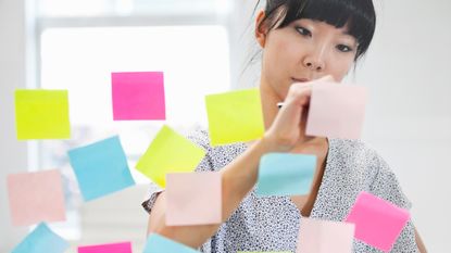 A woman makes notes on colorful Post-Its.