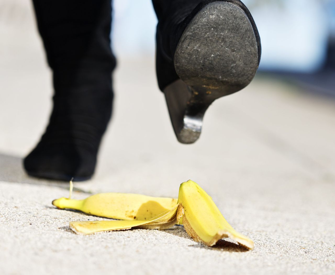 An unidentified female walker&#039;s foot in high-heeled boots is about to step on a dropped banana peel. A painful fall coming in 3, 2, 1...