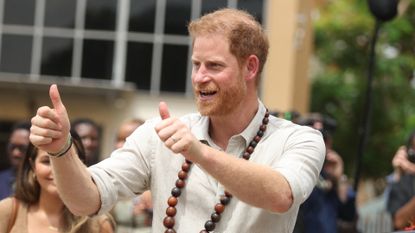 Prince Harry giving two thumbs up and wearing wooden necklaces