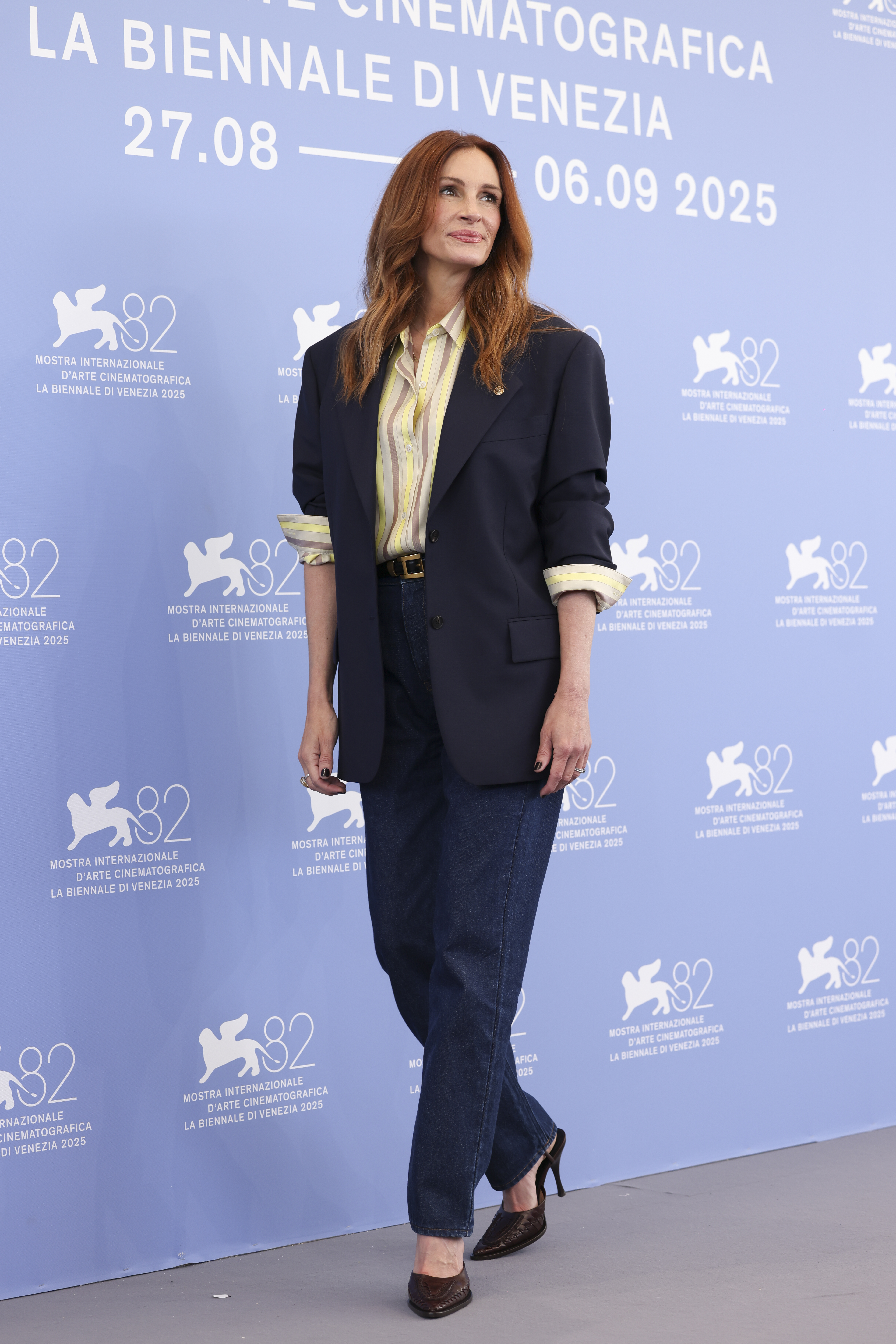 An image of actor Julia Roberts wearing a navy blue suit jacket over a yellow and pink striped shirt with indigo jeans and black heels at La Biennale Di Venezia in 2025