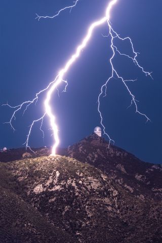 Lightning strikes over a mountain with observatories at twilight