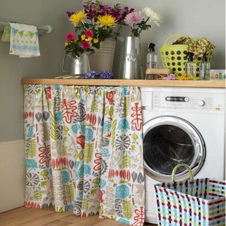 neutral kitchen utility area, 1950s style washing machine curtain skirt, laundry basket steel jugs as vases, with flowers