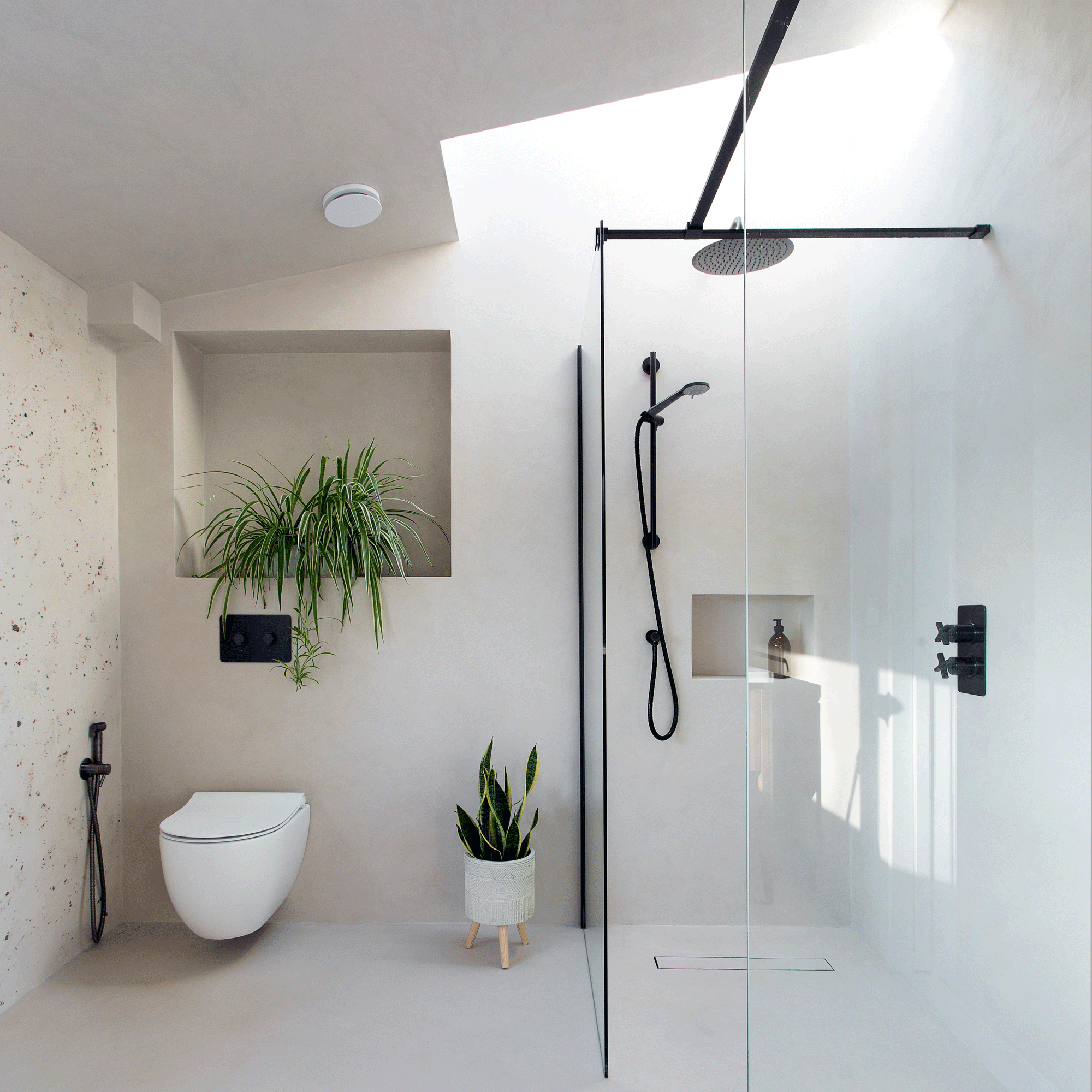 a neutral bathroom with a glass fronted shower a wall hung loo and house plants