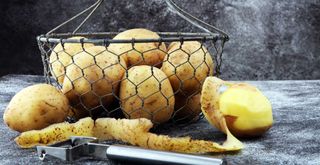 wire basket with potatoes with a stainless steel peeler