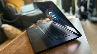 Asus ROG Zephyrus M16 gaming laptop open from the side sitting on a wooden table